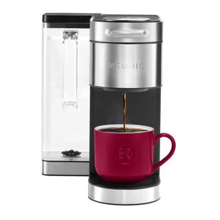 A silver and black Keurig K-Supreme Plus Coffee Maker with a red mug on it