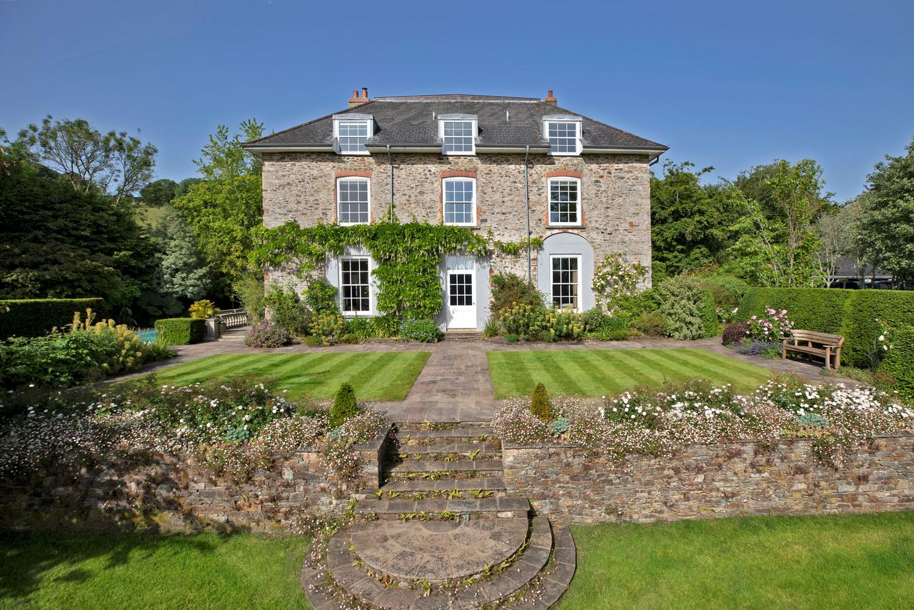 A view of the outside of the property with a stone wall in the foreground and lawned gardens