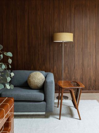 Lounge area with blue couch next to long lamp with golden shade in front of wooden paneled wall