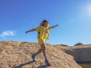 A woman smiling while hiking and wearing a yellow outfit with socks and sandals