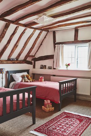 twin bedroom with exposed timbers and grey painted beds and red covers with christmas presents