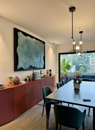 A dining room with teal chairs and a red console