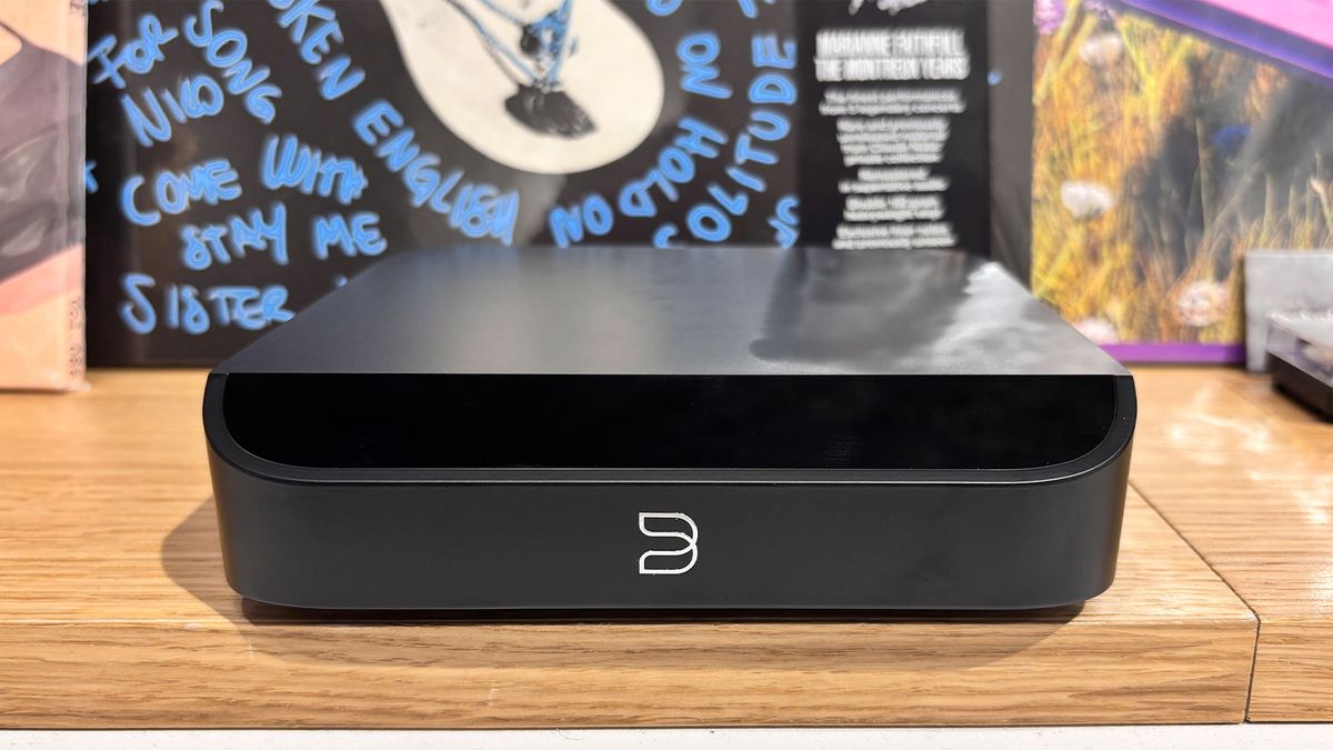 Bluesound Node Nano music streamer on wooden shelf with busy background