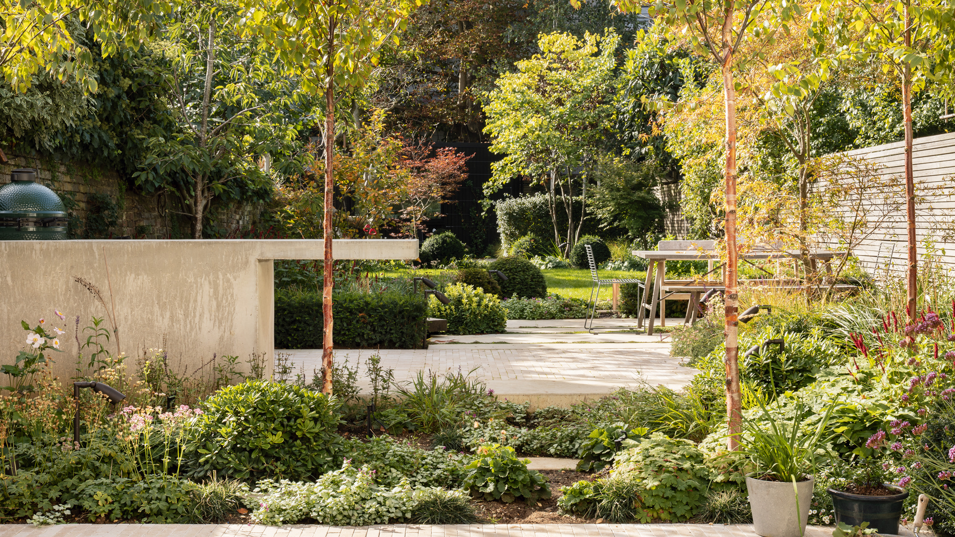 Tiered garden with pale stone and glass patio, pale brick steps and pale concrete outdoor kitchen
