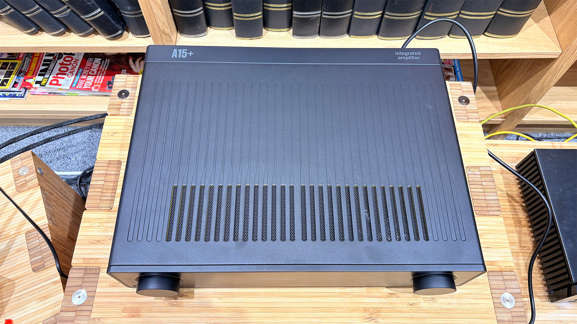 Arcam A15+ integrated amplifier on wooden AV rack in front of bookcase, top down view