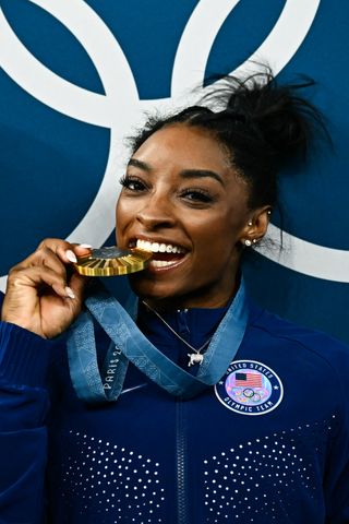 Simone Biles bites her Olympic gold medal while wearing her goat pendant necklace