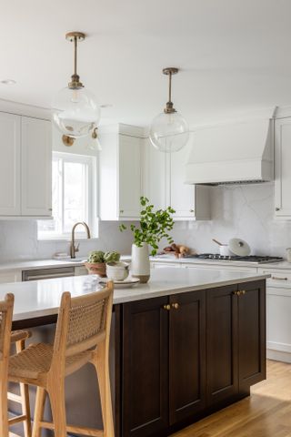 A white kitchen with white cabinets, a large island, and glass globe pendants and a glass wall light, both with brass hardware