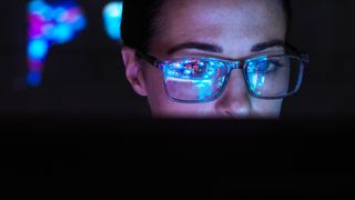 Female software developer working at computer with screen light reflecting in spectacles.