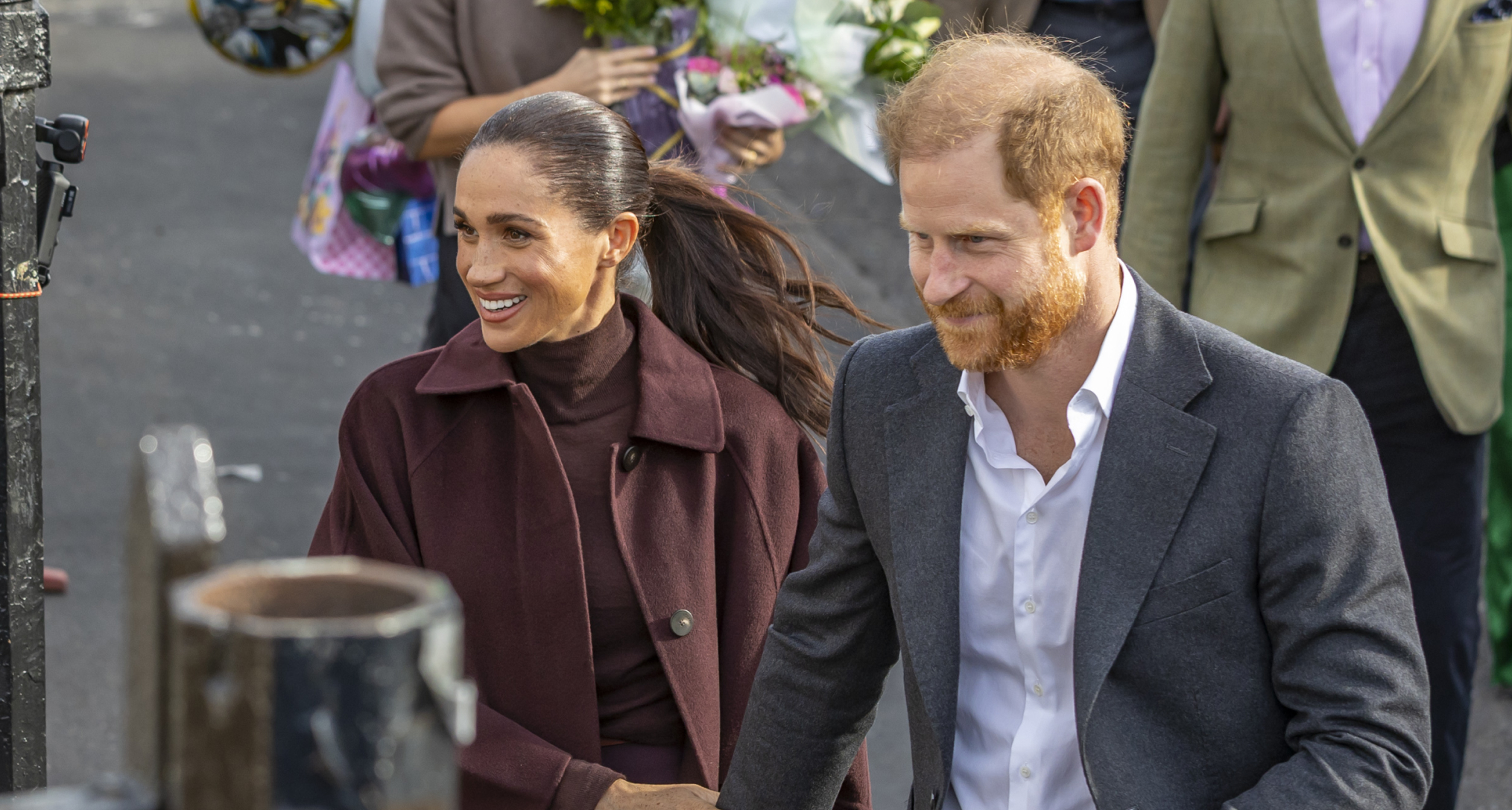 Meghan Markle wearing a maroon coat holding Prince Harry's arm