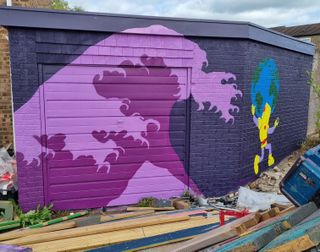 A garden shed painted with a purple wave and a yellow robot holding up a globe