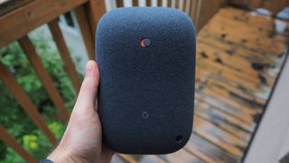 The Nest Audio speaker held in hand, outside on a deck.