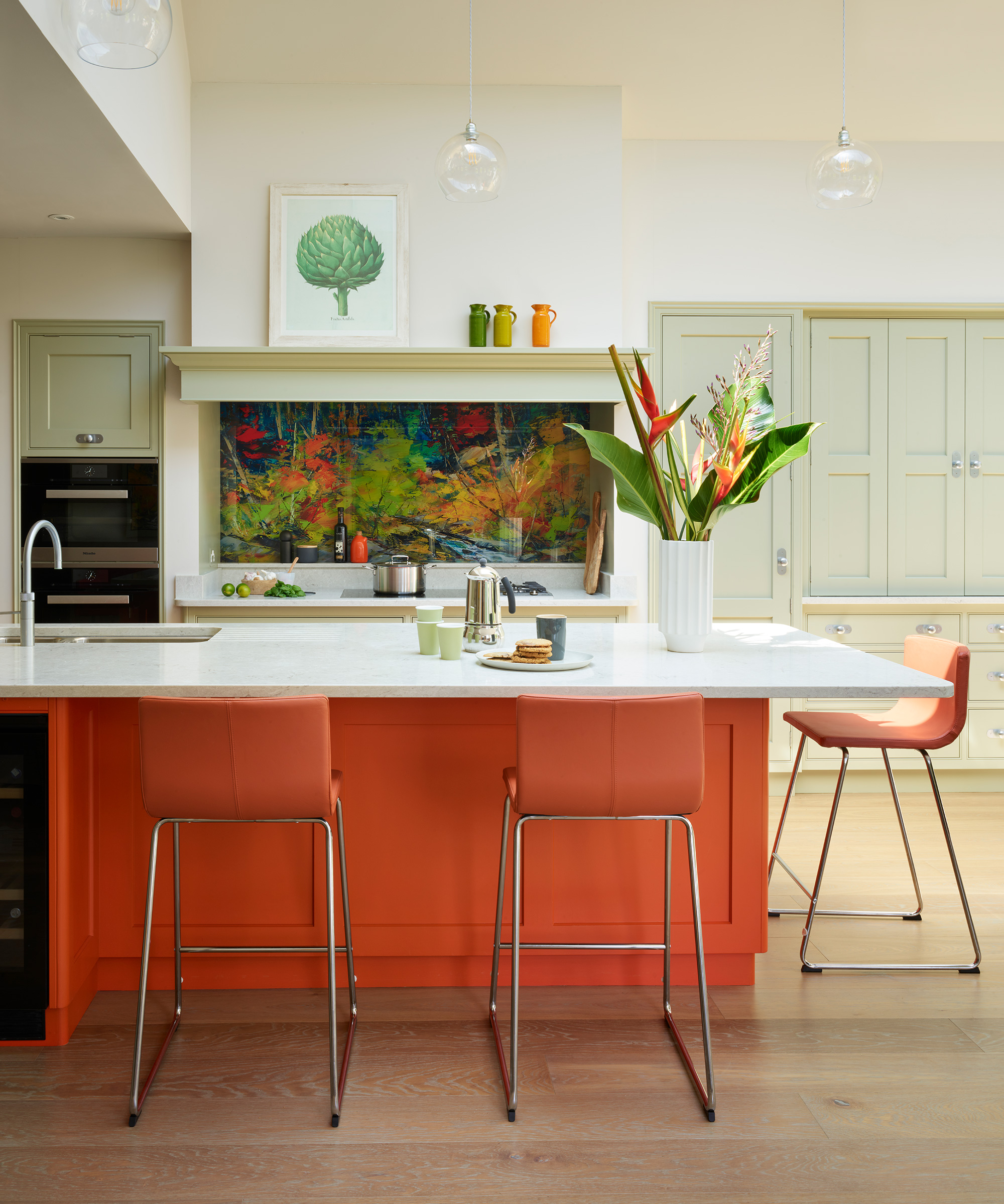 An orange island with a white worktop and contrasting green plants and artwork