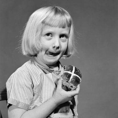 Black and white image of a girl eating a hot cross bun