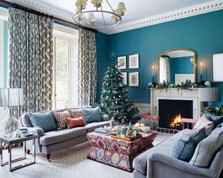 Elegant living room with blue painted walls, two gray sofas, christmas tree decorated with blue decorations