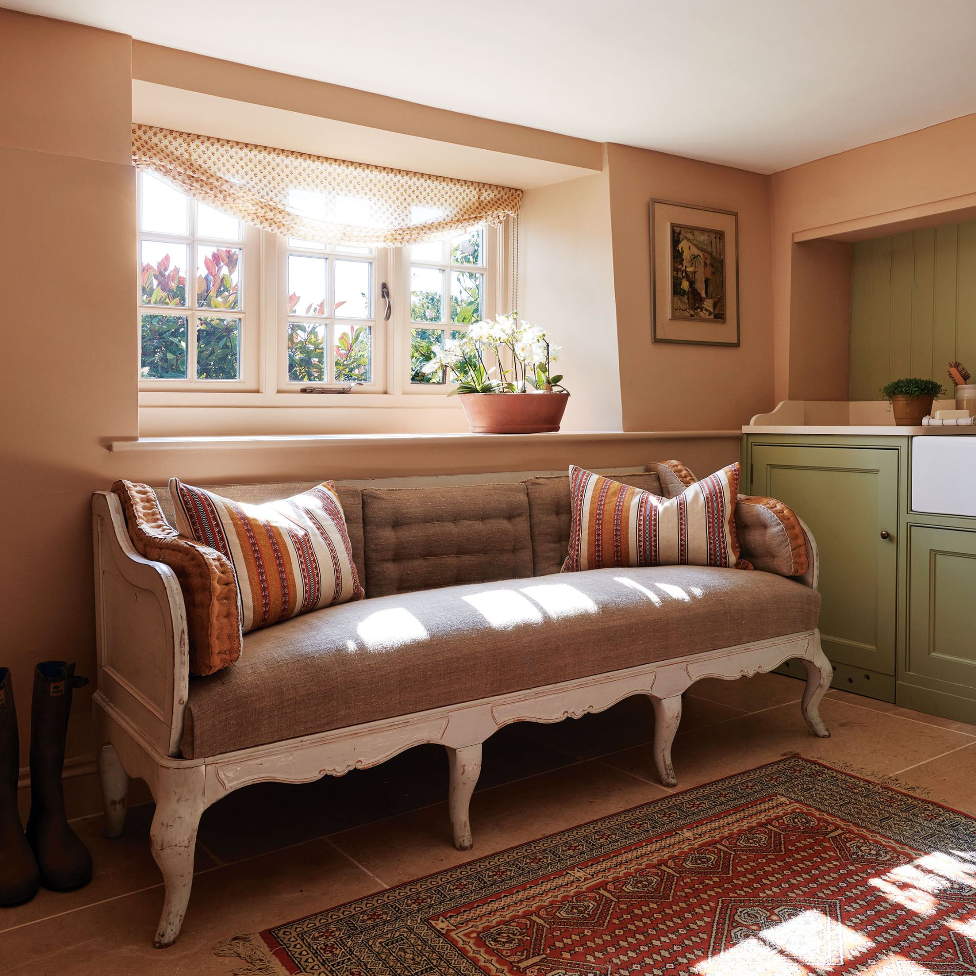 Boot room in dusty pink with green cabinets, sofa and rug
