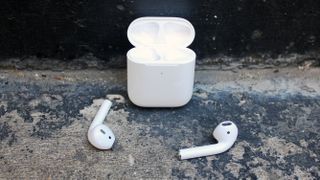 Apple AirPods liggende på bakken sammen med ladeetuiet