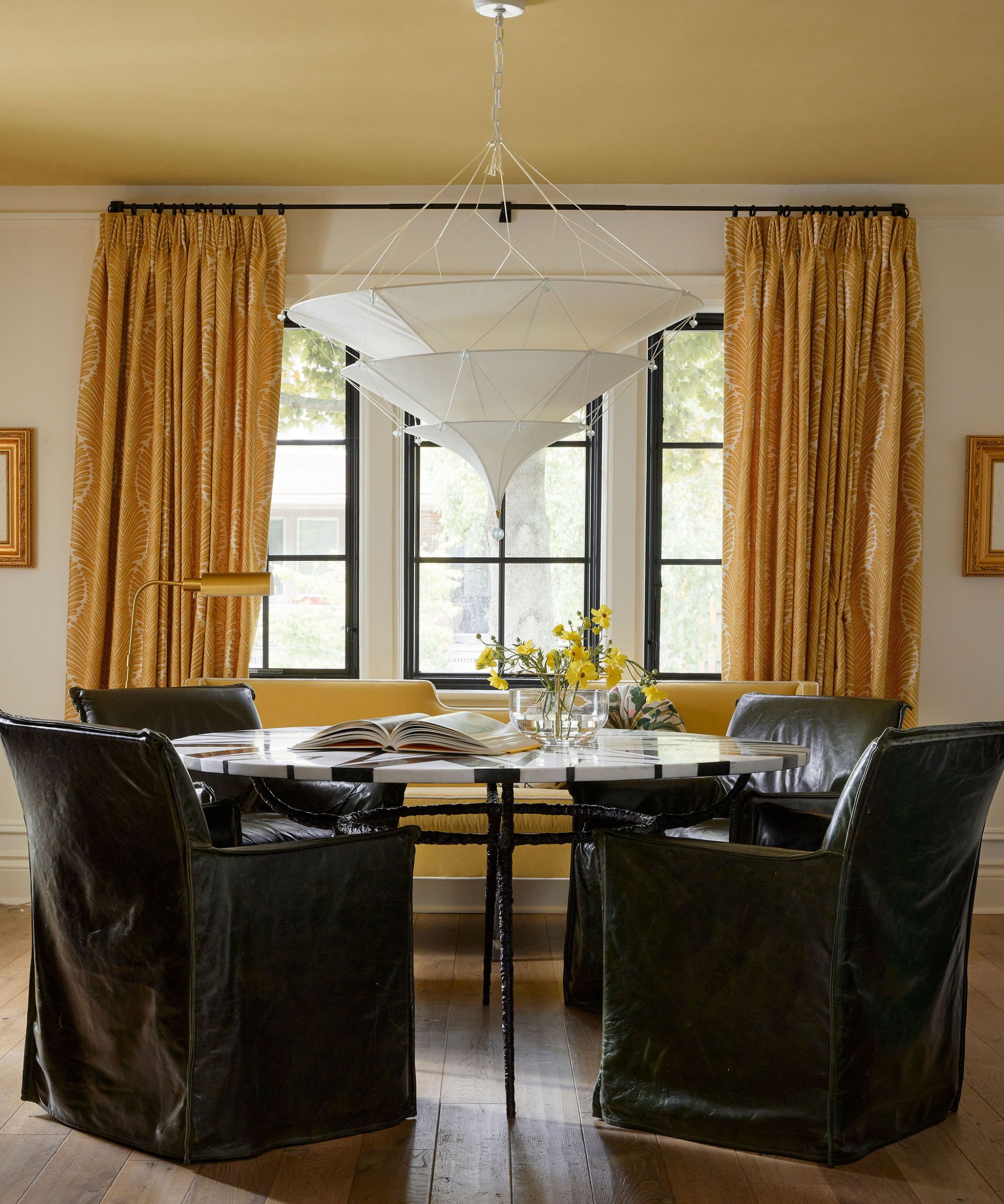 Yellow dining room with a round marble dining table and large leather armchairs around. A statement white pendant light hangs above