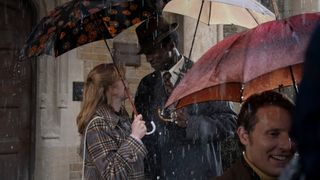 Cyril and Rosalind lean in for their first kiss in the rain and standing under umbrellas