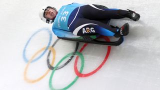 Luge competitor hurtles past the Olympics symbol at Beijing 2022