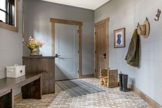 foyer with brick floor gray painted paneled walls bench and coat hooks