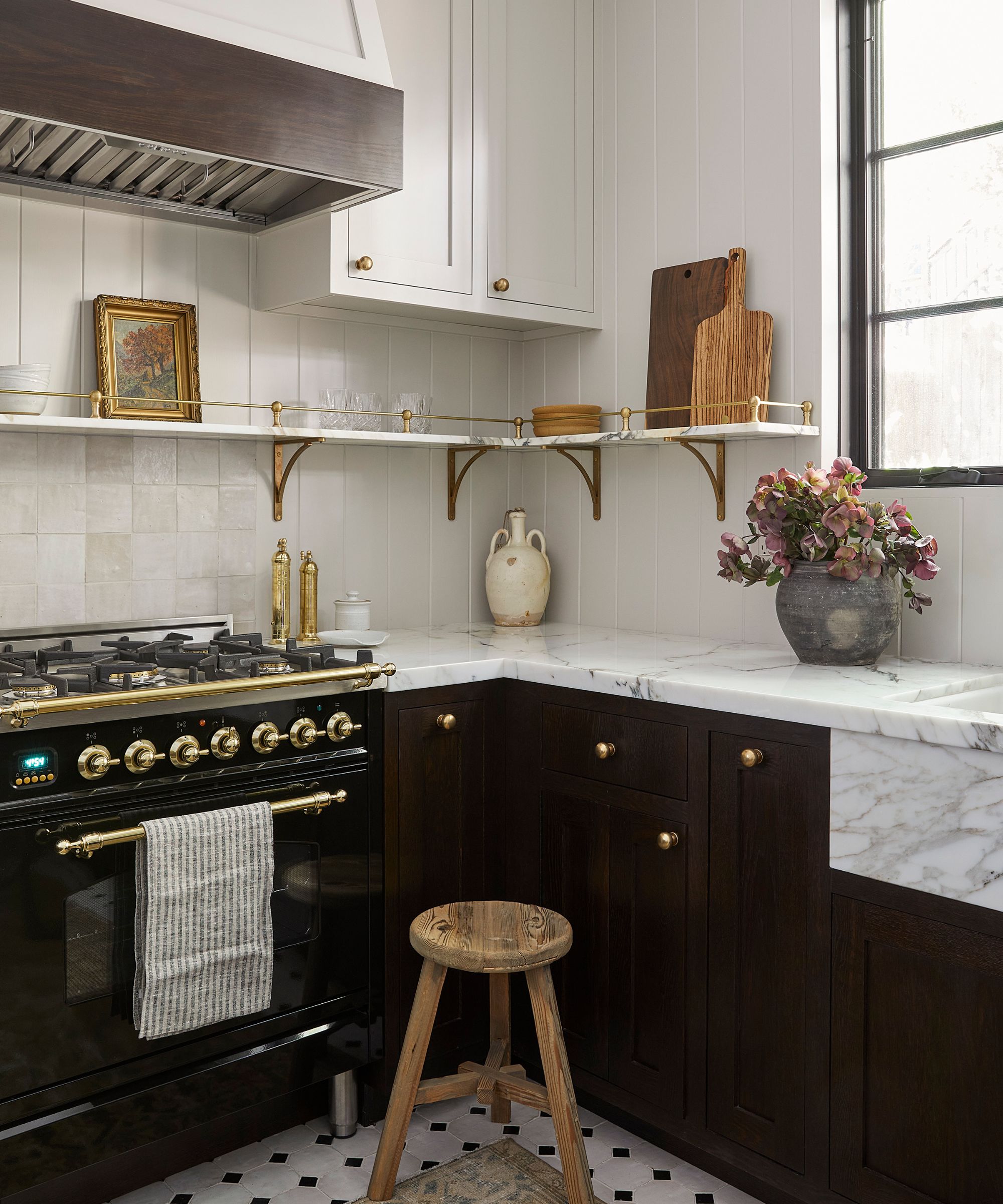 Corner kitchen view showing a black and brass gas range, white marble counters, dark lower cabinets, and open shelving.