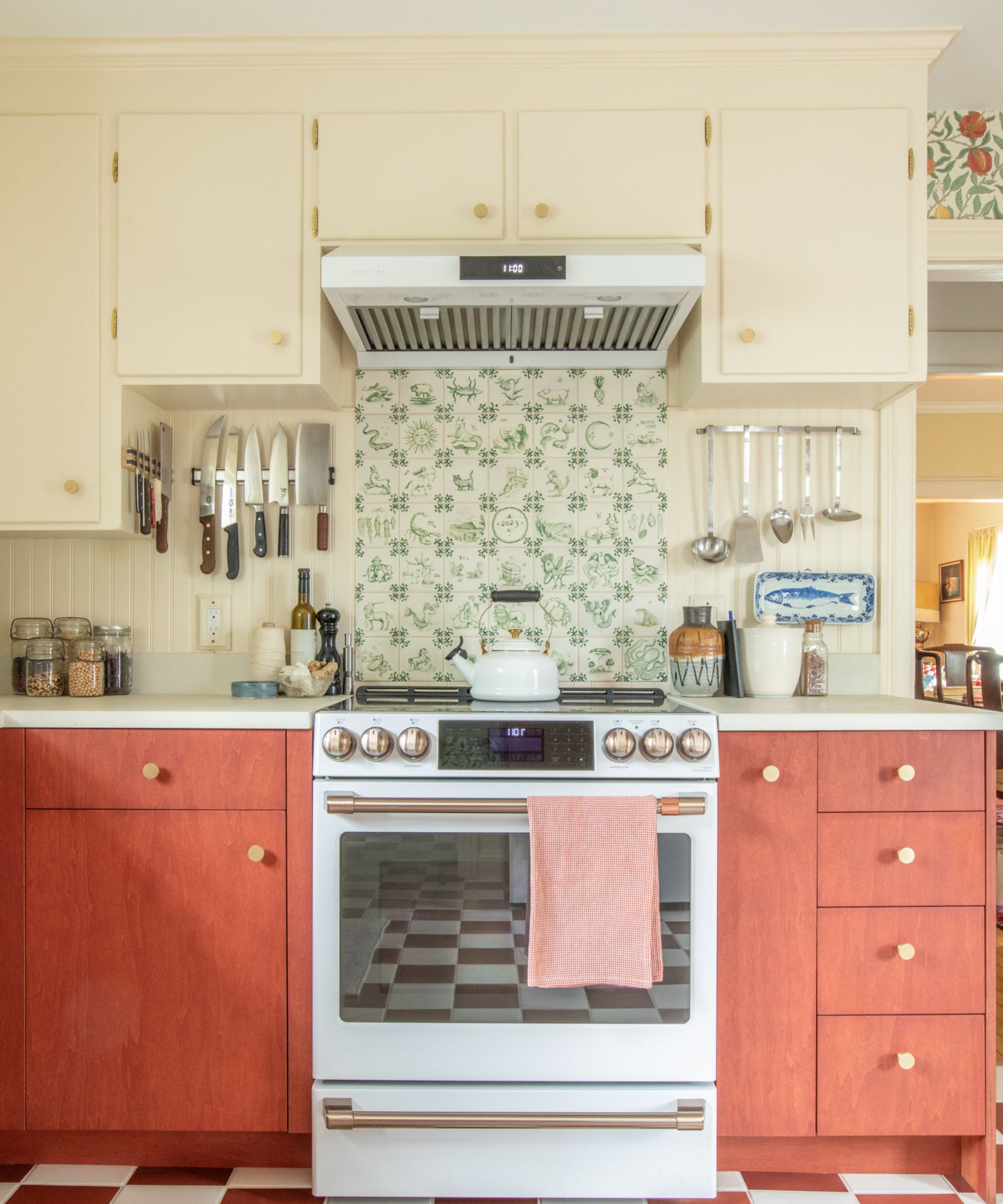 Eclectic kitchen view of a white stove surrounded by reddish-brown cabinets and a unique green-and-white illustrated tile backsplash.