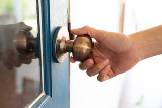 Person holding front door knob on a blue door