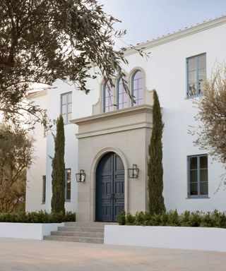 Raised front yard flower bed ideas in front of an imposing stone facade flanked by cypress trees.