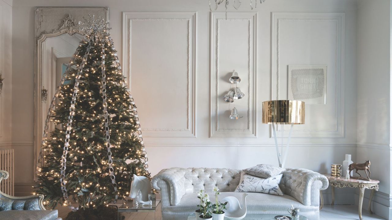 Ice blue classic button sofa with large Christmas tree with soft warm lights and ribbons running down from the top. Walls have paneling and the room is bright 