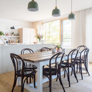 A kitchen diner with wooden dining table set with trio of sage green pendant light fixtures overhead