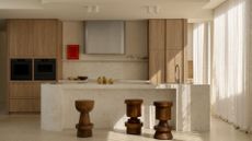 A warm and beautiful kitchen with a stone backsplash and kitchen island, along with a set of three sculpted wooden stools
