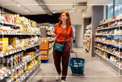 woman looking at shopping list in supermarket while pulling a basket trolley