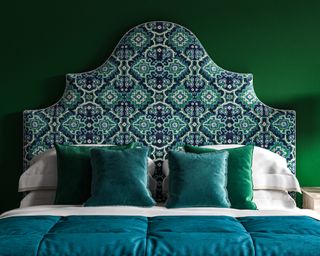 A dark green example of apartment bedroom ideas with a large upholstered headboard in a blue, white and green patterned velvet