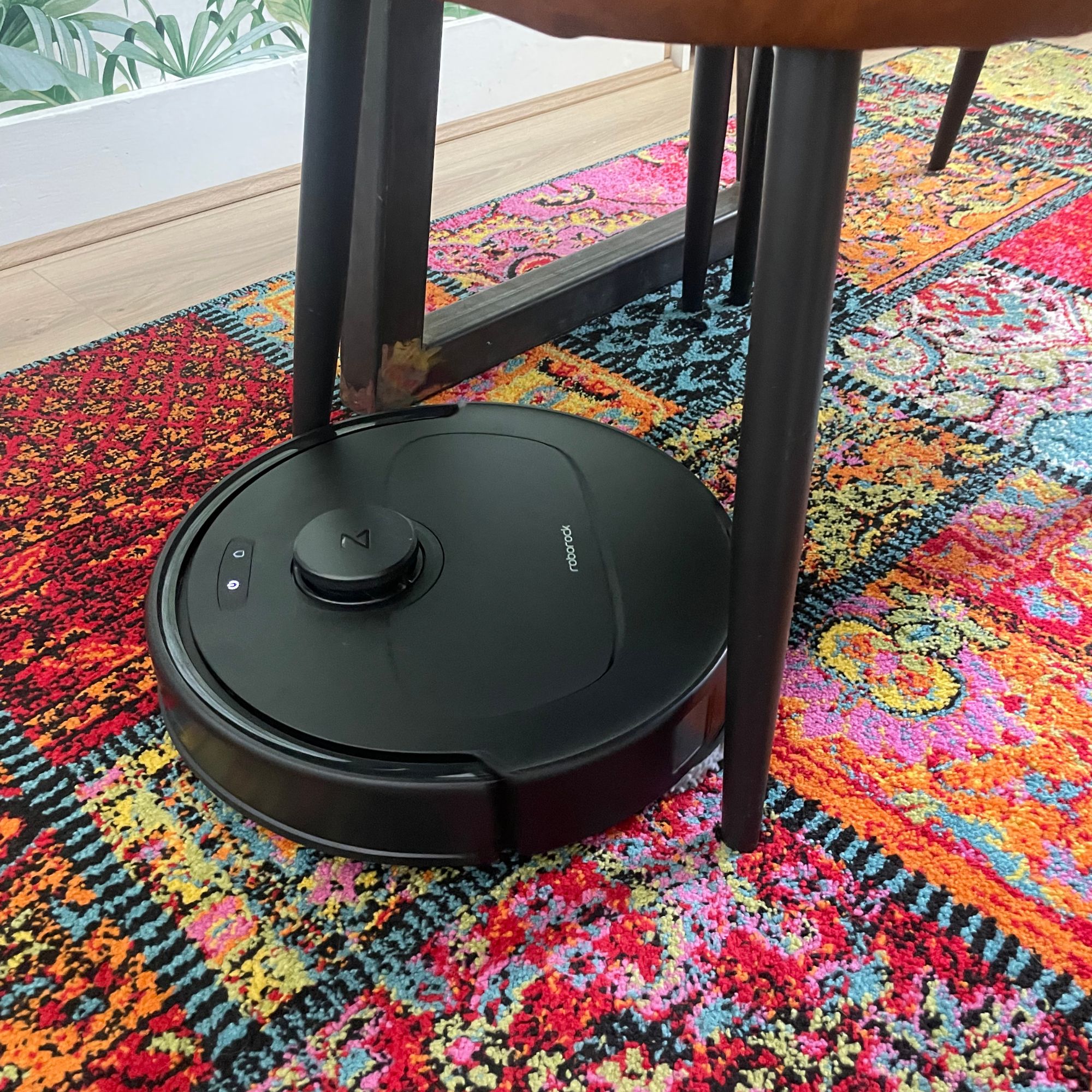 Roborock QV 35S Robot Vacuum With Mop cleaning in between chair legs on a colourful rug