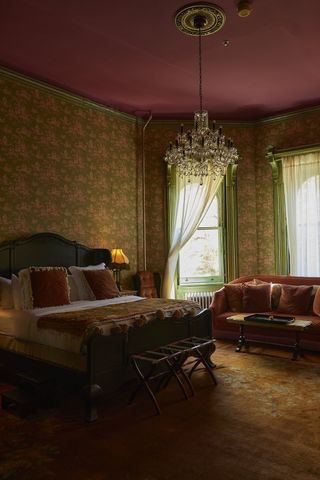 A vintage-looking bedroom in a hotel features glassy chandeliers and lavish decor throughout, all in bordeaux, soft pink, and green tones.