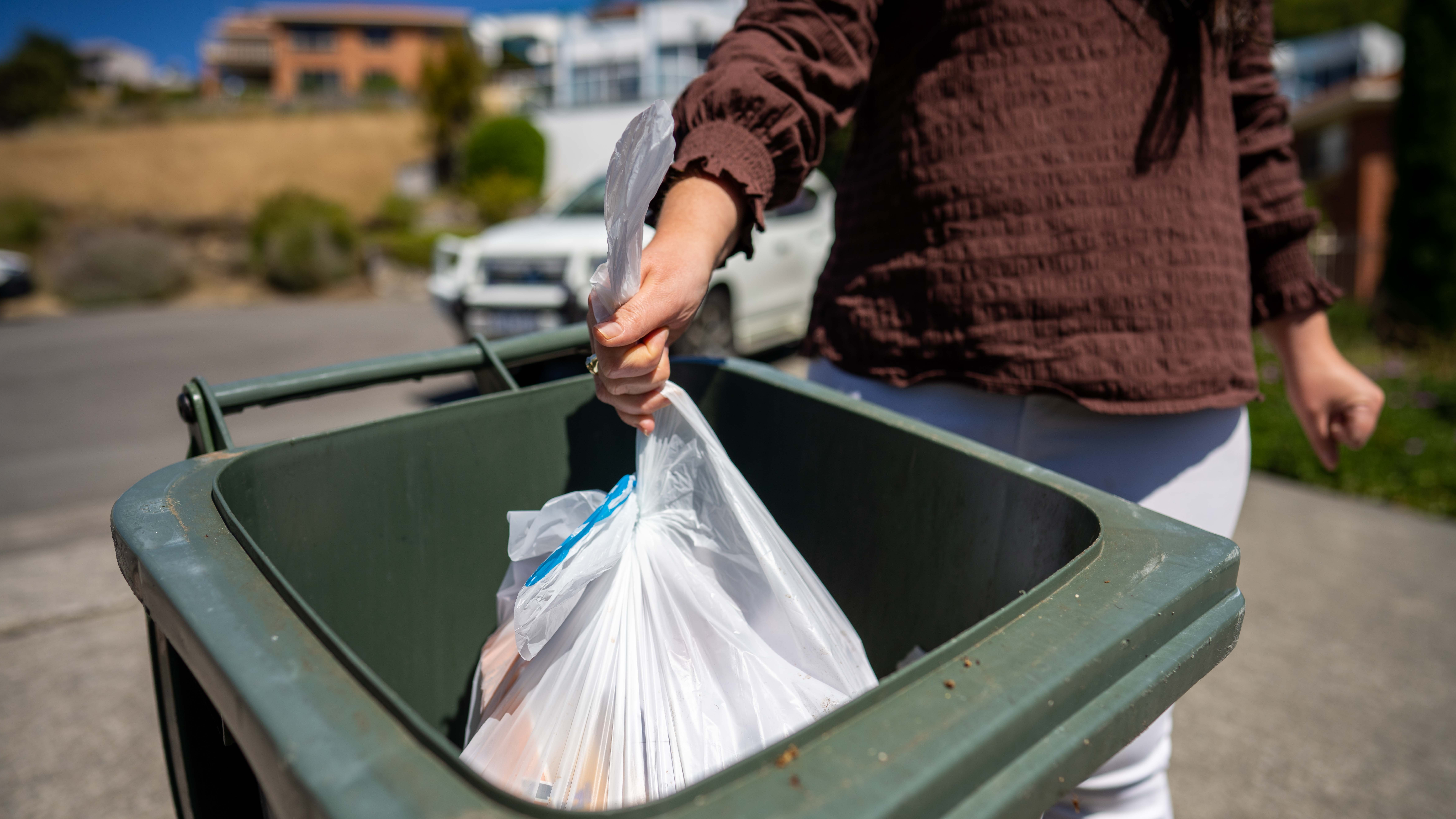 Putting trash bag into garbage bin outdoors