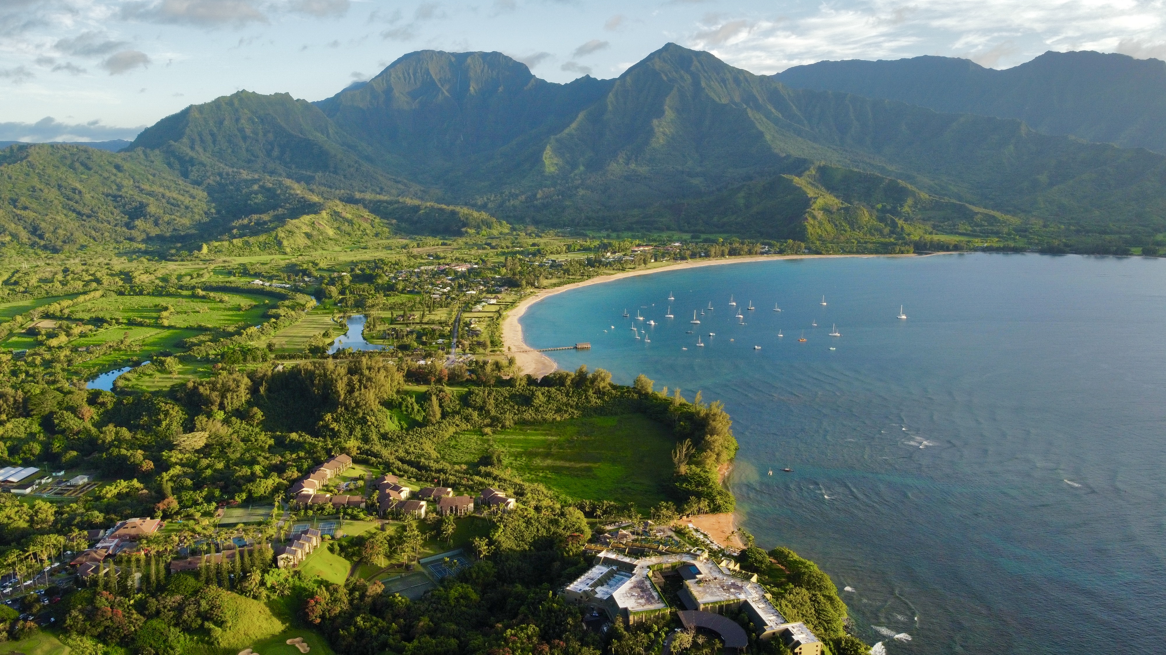 An aerial view of the beach and green mountains of Hanalei Bay