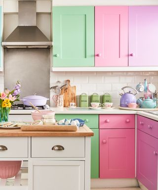 A colorful kitchen with mint green, pink, and purple cabinets, a silver oven hood, and a white portable kitchen island with flowers on top