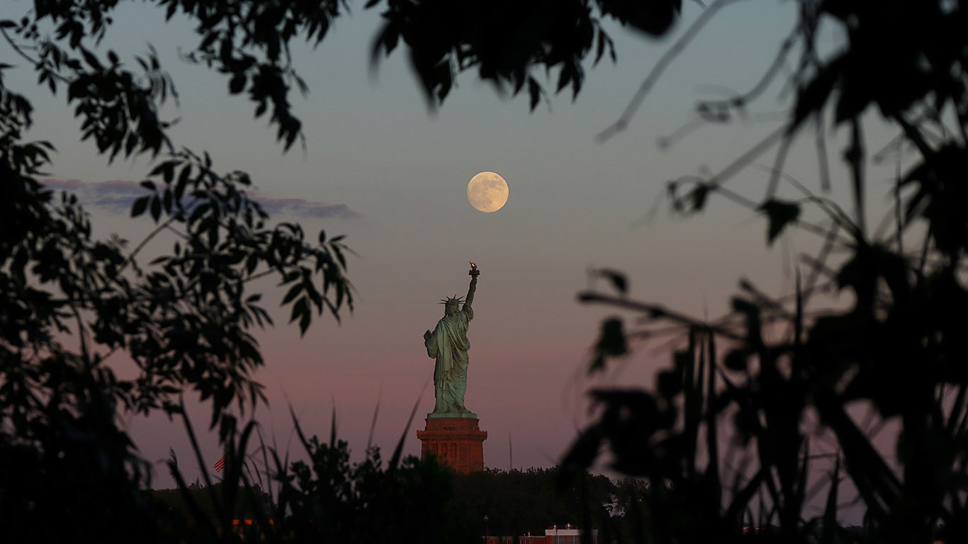 An almost full moon rises above the Statue of Liberty as the sun sets in New York City on June 23, 2021 as seen from Jersey City, New Jersey.