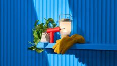 A glove, drill, plant and lantern sitting on a blue shelf on a blue wall.
