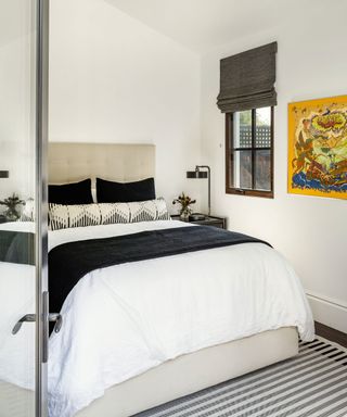 Monochrome bedroom with white painted walls, black and white bedding, black, cream and gray striped rug, bright yellow artwork