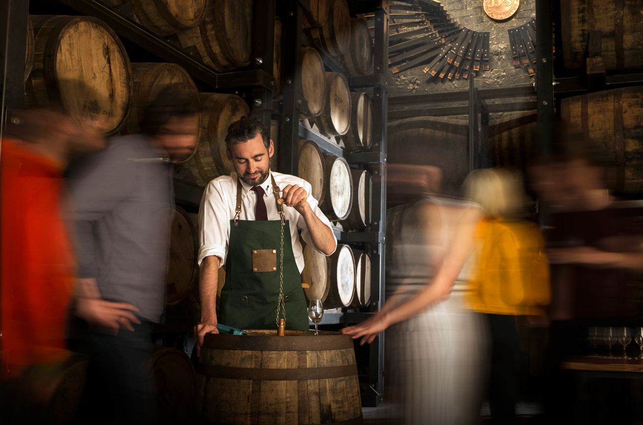 A man in an apron draws a sample of whisky from a cask