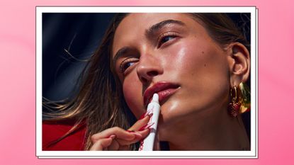 Hailey Bieber pictured with blushy, 'strawberry girl' makeup, whilst applying her new 'Strawberry-Glazed' Rhode Peptide Lip treatment/ in a pink gradient template