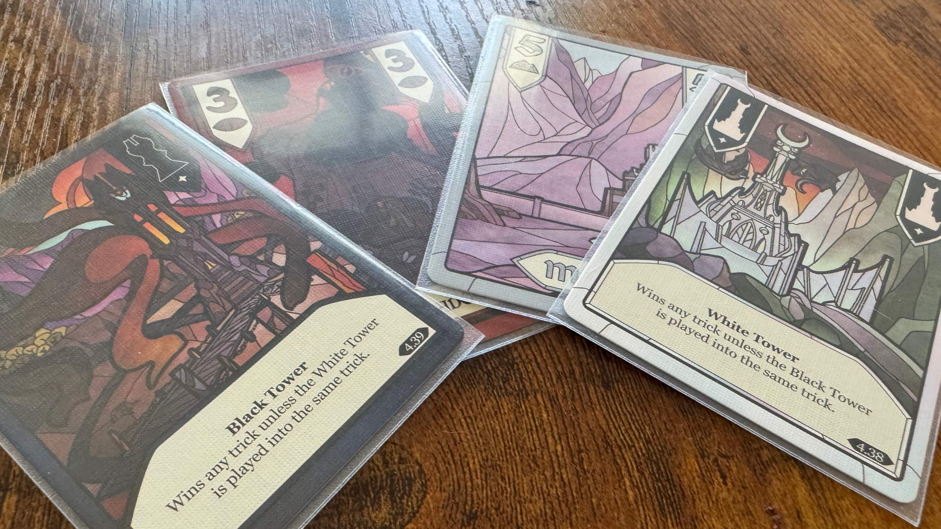 Cards from the Two Towers Trick-Taking Game laid out in a spread on a wooden surface
