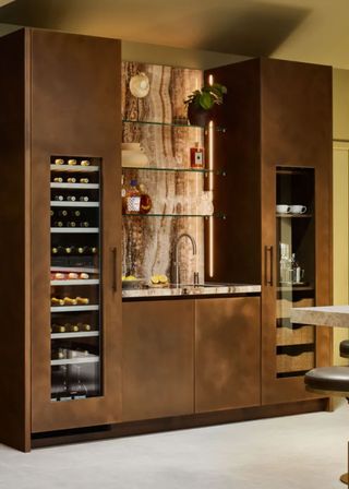 a bronze effect kitchen with bold marble counters, a glass fronted drinks fridge and coffee station