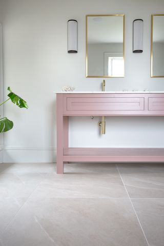 neutral bathroom with pink vanity unit, floor tiles, gold mirrors, wall lights