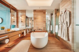 Bathroom with wood panels, oval white bathtub and hanging bathrobes