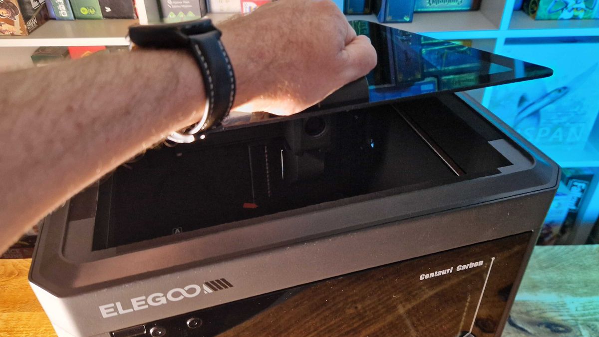 A hand lifting the lid of the Elegoo Centauri Carbon