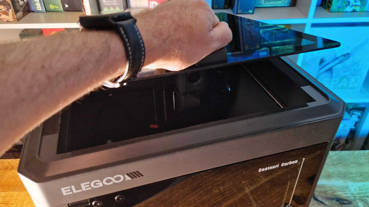 A hand lifting the lid of the Elegoo Centauri Carbon