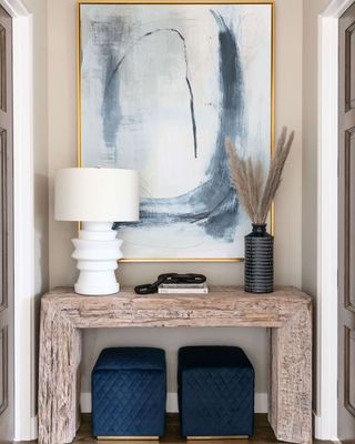 Cozy entryway with wooden console table, art work, greenery and table lamp